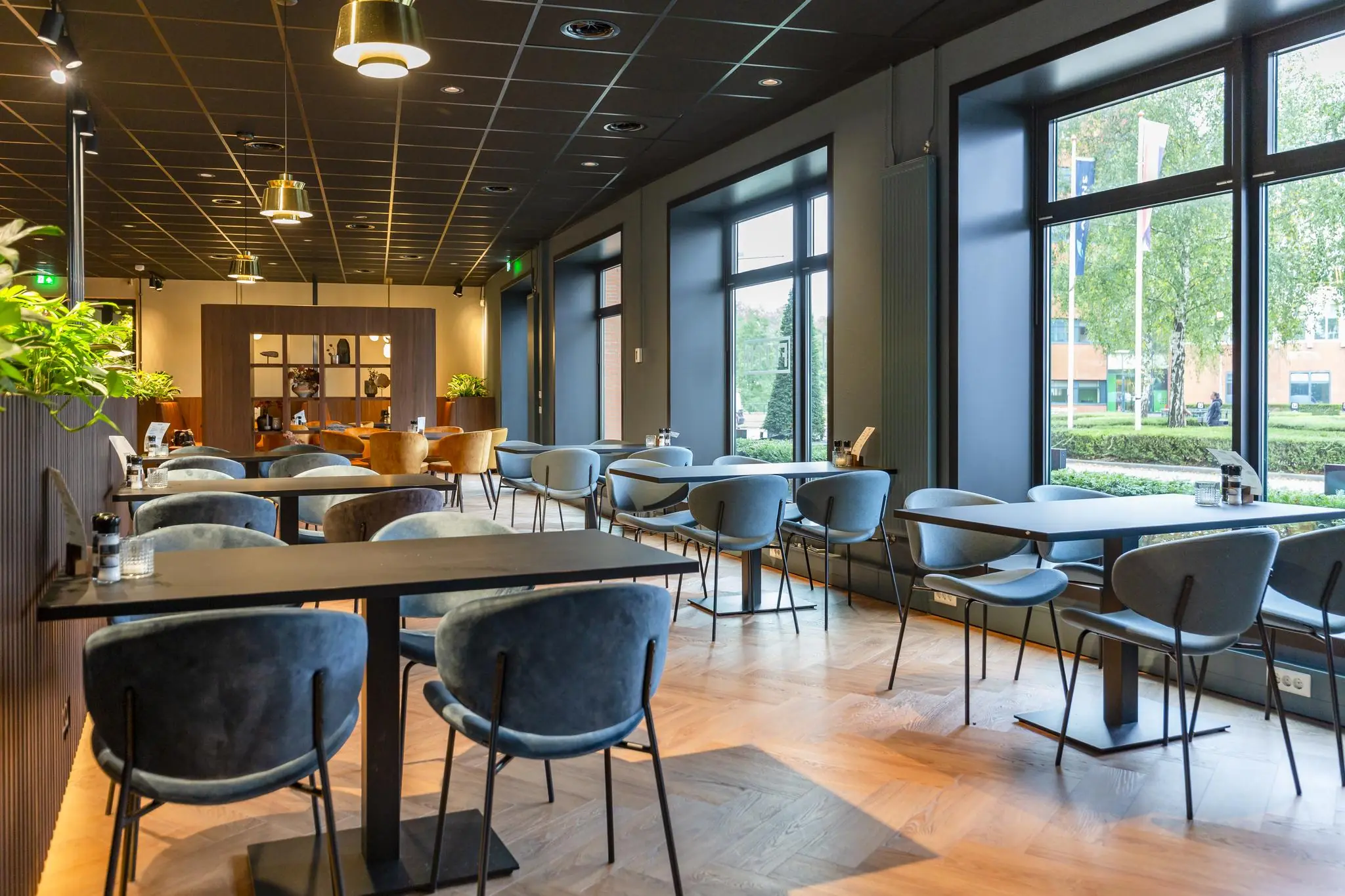 Modern ingericht restaurant aan de George Hintzenweg met ruime zitplaatsen en grote ramen met uitzicht op groen.